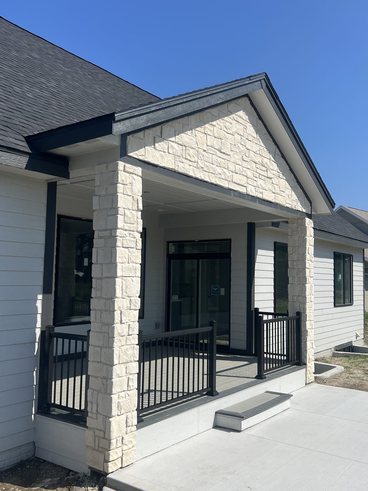 Covered entry deck with black metal railing and stone columns