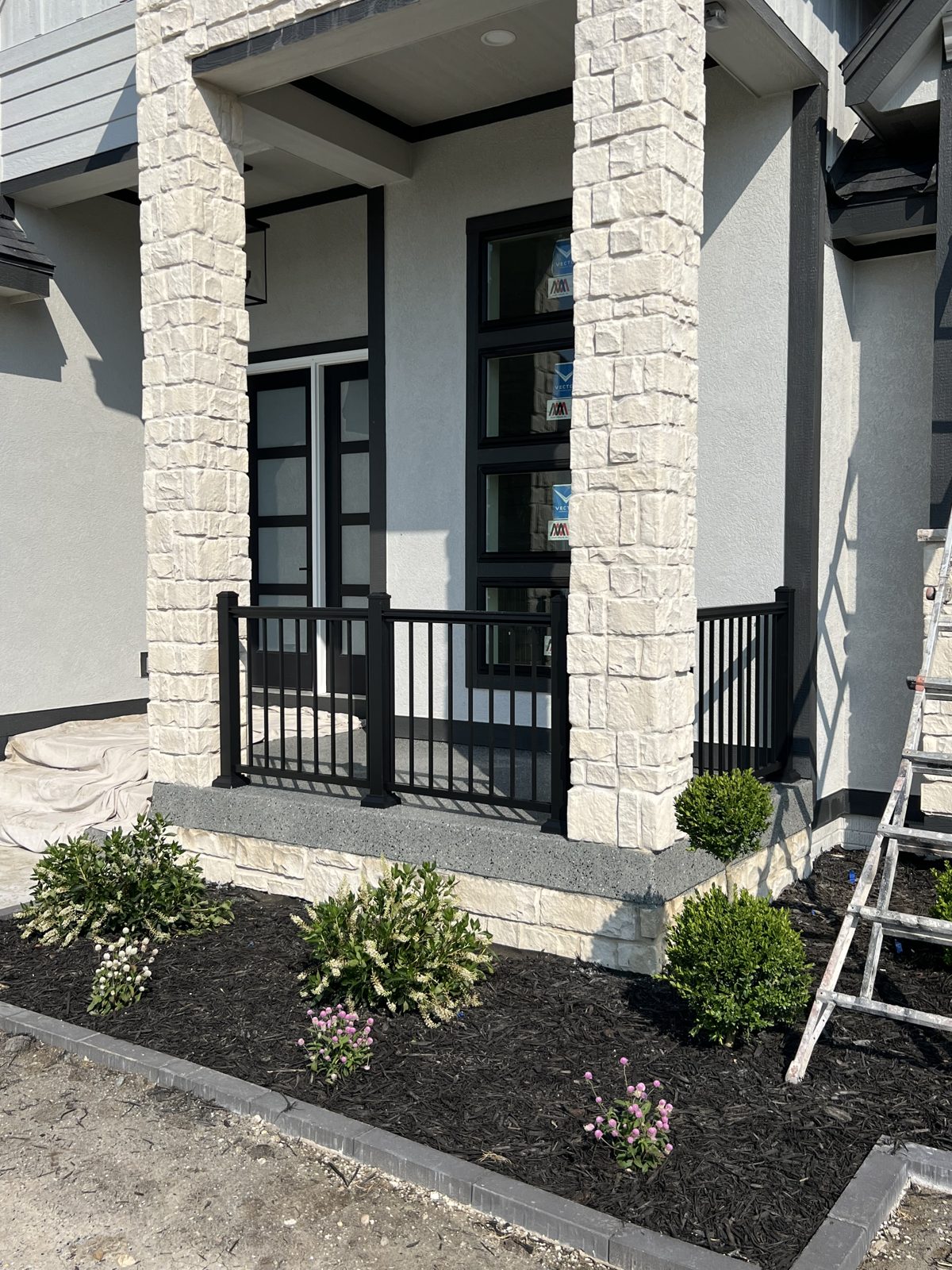 Covered porch corner with black metal railing and stone columns
